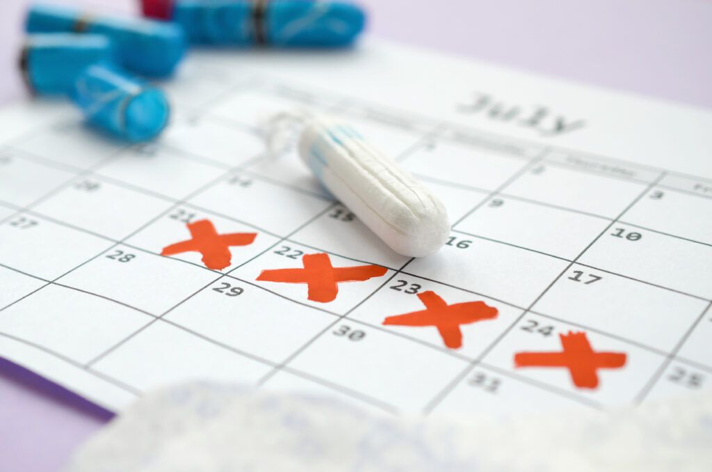 Menstrual pads and tampons on menstruation period calendar with red cross marks lies on lilac background