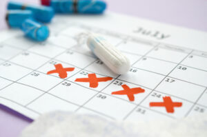 Menstrual pads and tampons on menstruation period calendar with red cross marks lies on lilac background