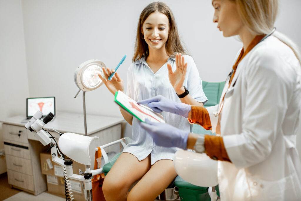 Gynecologist showing a picture with uterus to a young woman patient, explaining the features of women's health during a medical consultation in the office